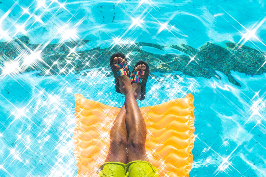 legs on a pool float over pool water wearing chaco chillos tiedye slide sandals