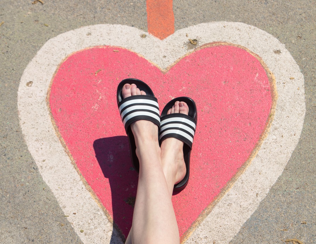 pink heart on pavement with women's legs wearing adidas slide sandals